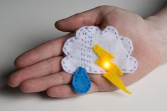 a hand holding a small felt toy with a lightning and cloud on it's palm