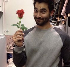 a man holding a rose up to his face and smiling at the camera while standing in front of a closet