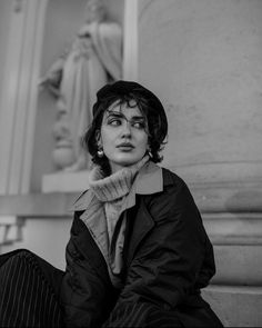 a black and white photo of a woman sitting on the ground next to a statue