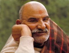 an older man with a goatee smiles while leaning on his hand to the side