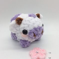 a crocheted stuffed animal next to a pink and white flower on a white surface