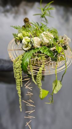 flowers and plants are arranged in a basket on a table with metal rods attached to it