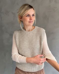 a woman standing with her arms crossed and looking at the camera while wearing a sweater