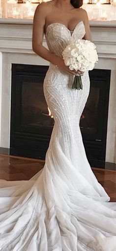 a woman in a wedding dress standing next to a fire place holding a bridal bouquet