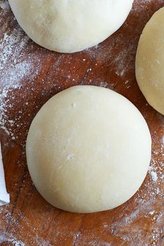 three uncooked doughnuts sitting on top of a wooden table covered in powdered sugar