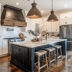 a kitchen with an island and three pendant lights hanging over the stove top, along with stools