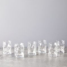 five clear glass tumblers lined up in a row on a gray surface with white wall behind them