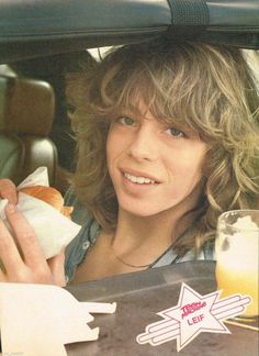 a woman sitting in the back seat of a car holding a hot dog and drink