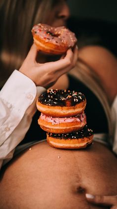 a pregnant woman holding three donuts on her belly