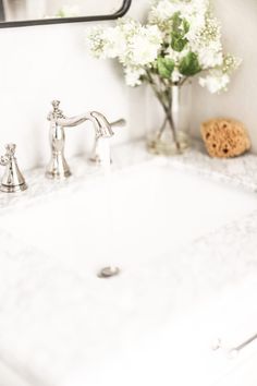 a white sink sitting under a bathroom mirror next to a vase with flowers in it