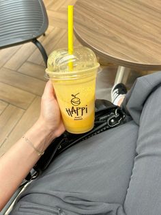 a person holding up a cup with a yellow drink in it on top of their lap