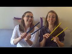 two women sitting on a couch holding up sticks