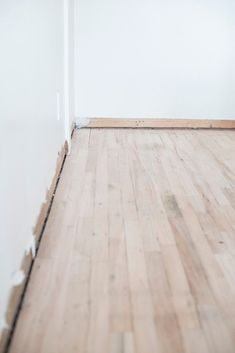 an empty room with white walls and wood flooring that is being installed on the wall