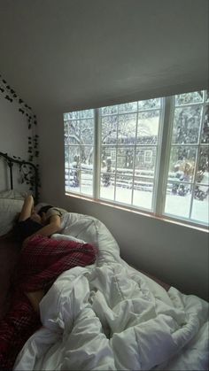 a person laying on a bed in front of a window with the snow outside it