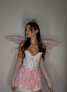 a woman dressed as a fairy with wings on her head and pink dress, standing in front of a white wall