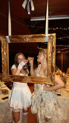 two women standing next to each other in front of a framed photo with candles on it