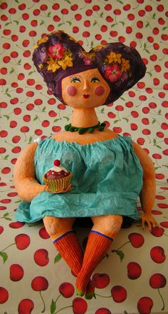 a doll sitting on top of a bed holding a cupcake