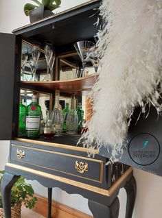 a black and gold cabinet with wine glasses on it's shelves, next to a potted plant