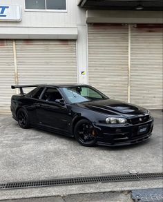 a black sports car parked in front of a garage with roller doors on the side