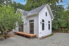 a small white house sitting in the middle of a yard with trees around it and a picnic table