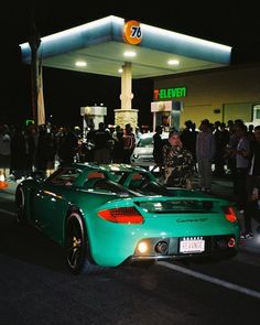 two green sports cars parked in front of a gas station at night with people standing around