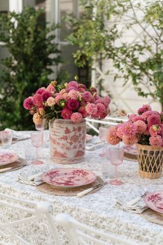 the table is set with pink and white plates, cups, and vases filled with flowers