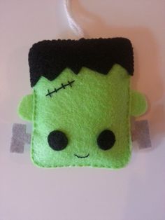 a green felt ornament hanging from a white cord with a black head and eyes on it