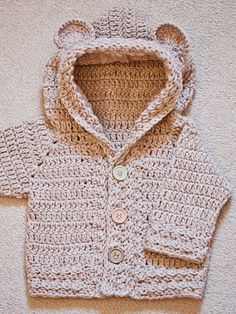 a crocheted sweater with a hood and buttons on the front is shown in beige