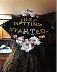 a woman wearing a graduation cap that says just getting started with flowers on the side