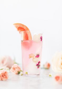 a pink drink with orange slices and flowers on the table next to it's garnishes