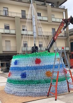 a man on a ladder working on a sculpture made out of empty water bottles in front of a building