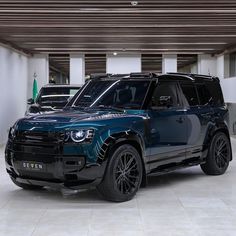 two suvs are parked in an empty parking garage, one is blue and the other is black