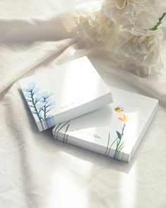 two business cards sitting on top of a bed next to a bouquet of white flowers