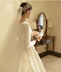 a woman in a white wedding dress holding flowers and looking at herself in the mirror