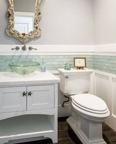 a white toilet sitting next to a sink in a bathroom under a large round mirror