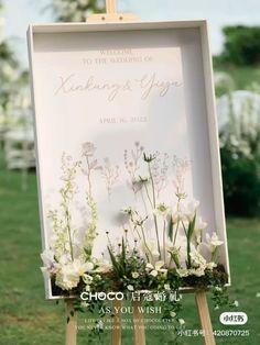 an easel with flowers and greenery on it in front of a wedding sign