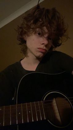 a young man with curly hair playing an acoustic guitar