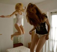 two women jumping in the air over a bed