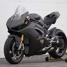 a black motorcycle parked in front of a white brick wall with wheels on each side