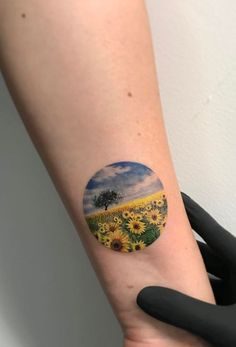 a woman's arm with a sunflower and tree tattoo on the left forearm