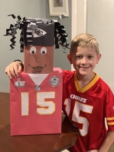 a young boy holding up a paper bag with a football jersey on it