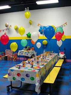 a birthday party setup with balloons and streamers on the wall, table cloths