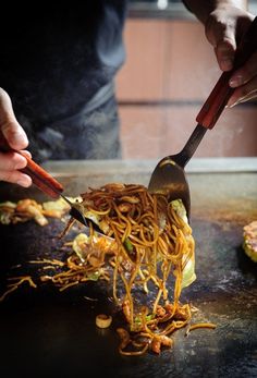 someone using tongs to stir noodles on top of a table with other food items