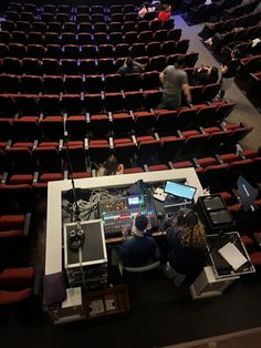 people are sitting in the middle of an auditorium with red chairs and electronic equipment on them