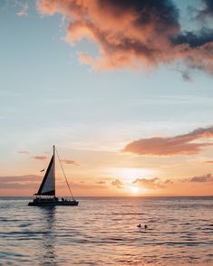 a sailboat floating in the ocean at sunset with people swimming around on the water