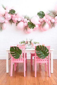 a dining room table with pink chairs and large green leaves on the wall above it