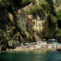 the beach is crowded with people and umbrellas in the shade, near some cliffs