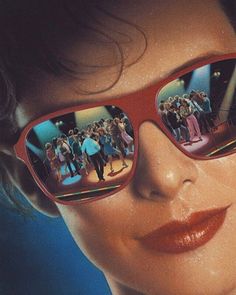 a woman wearing red sunglasses with people reflected in the glasses on her face and behind her is a blue background