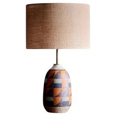 an orange and blue ceramic table lamp with a beige linen shade on the top of it