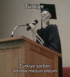 a skeleton wearing a graduation cap and gown stands at a podium in front of a microphone